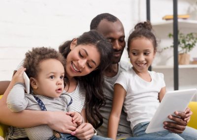 Happy Young Family Spending Time Together With Devices At Home