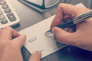 hands writing check at desk with pen