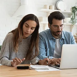 Pareja sentada en una mesa con una computadora portátil, facturas de alquiler y una calculadora, trabajando en un presupuesto