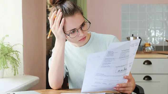 Mujer joven estresada con gafas, estudiando la documentación de un préstamo estudiantil