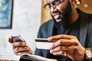 Man with glasses and watch holding credit card, entering information on phone