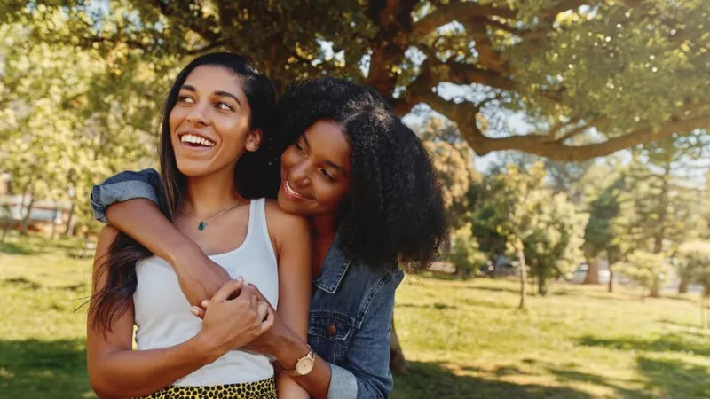 Two women hugging in-front of a tree.