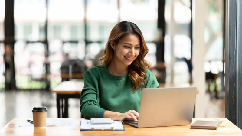 woman on laptop in office with coffee, laptop, and notepad