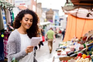 woman shopping in open stall market looking at shopping list