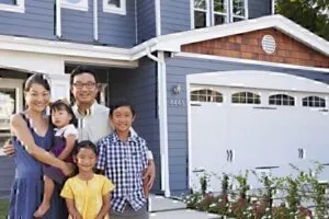 Asian family standing in front of blue residential house smiling at camera