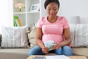 Pregnant Woman in t-shirt on couch, holding checks, bills, receipts