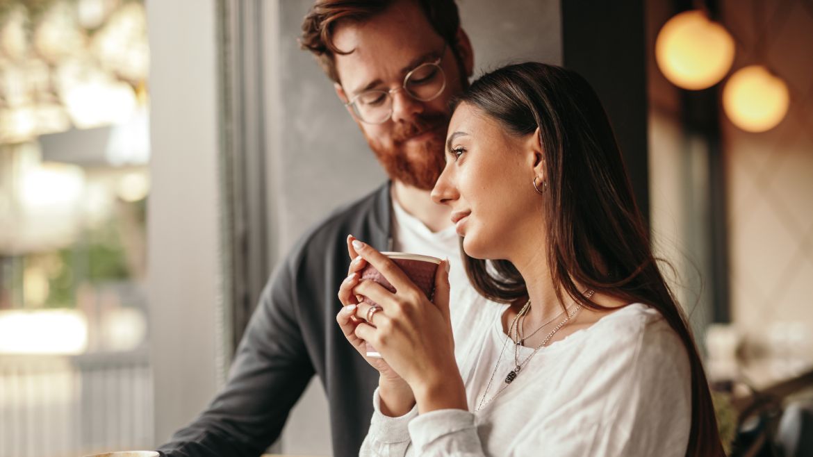 A white couple having coffee in their kitchen looking out the window.