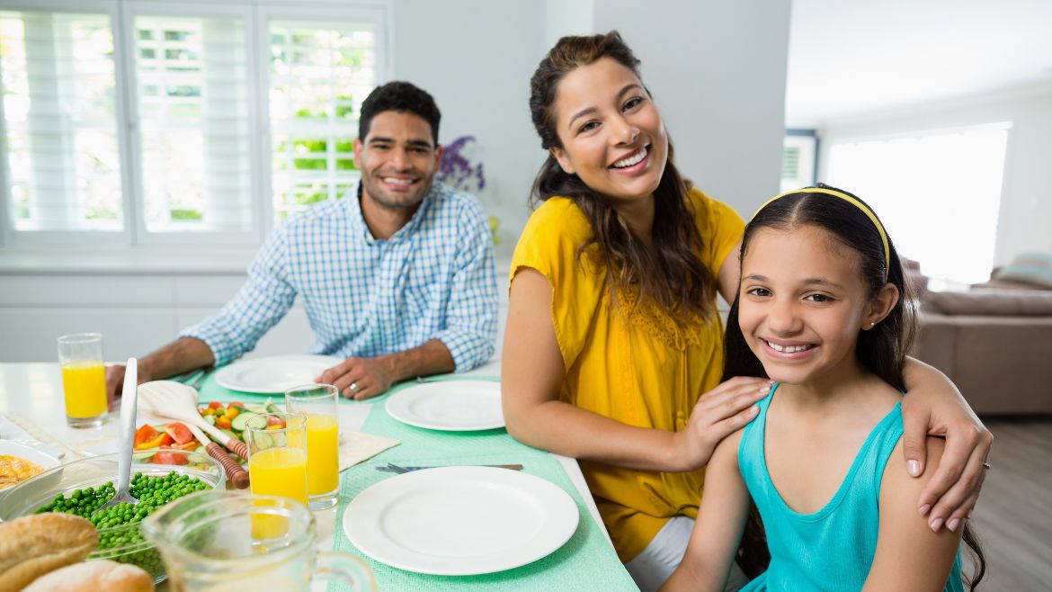 a family of three having dinner and smiling at the camera