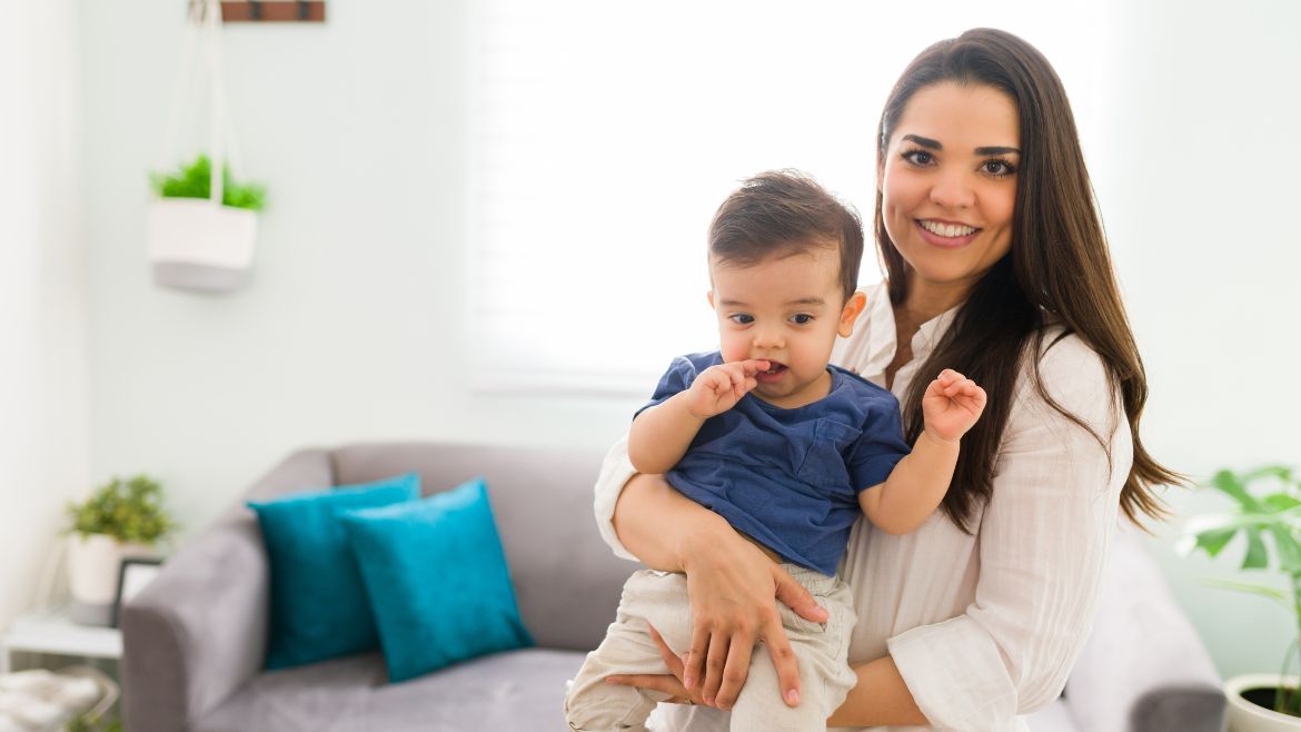 A young Latina mother holding her baby boy smiling faintly into the camera