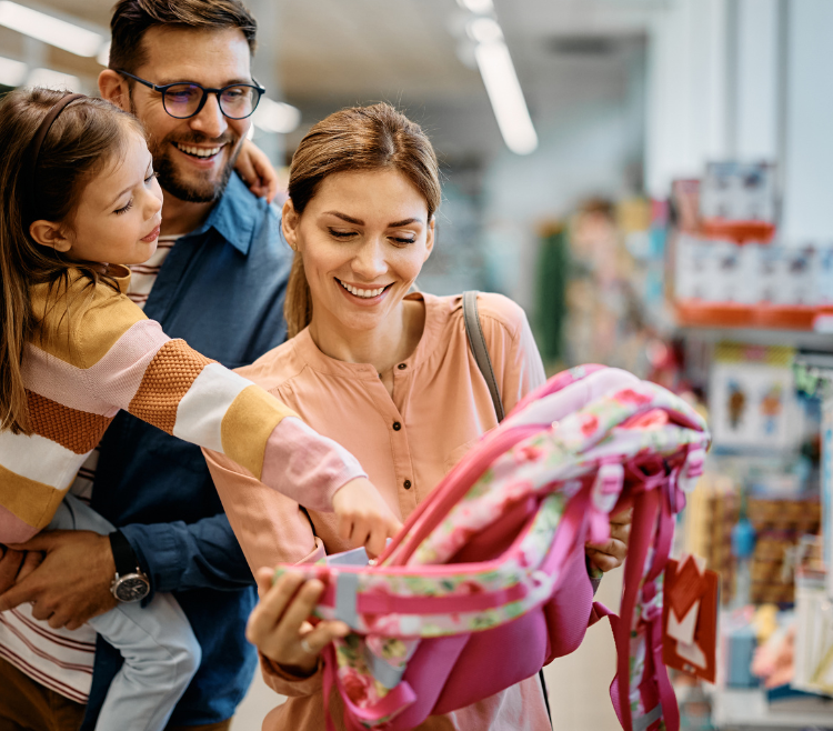 Little girl and her parents choosing backpack for school while shopping in store together.