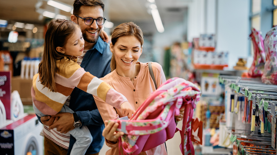 La niña y sus padres eligen la mochila para la escuela mientras compran juntos en la tienda.