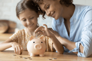 mom teaching daughter how to save money using a piggy bank