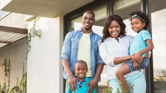a family of four standing in front of their new home.