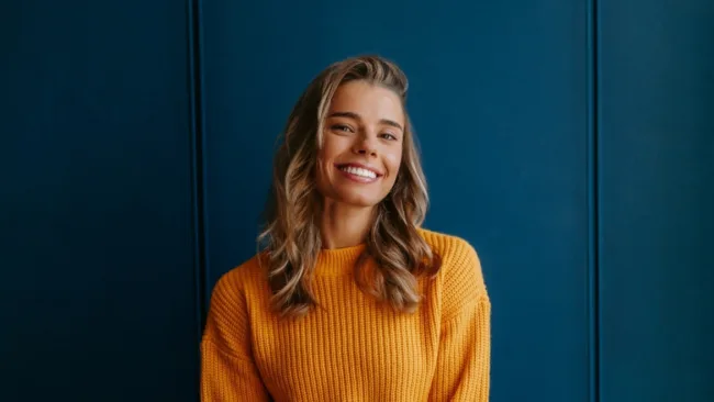 Woman smiling broadly standing in-front of a dark blue wall