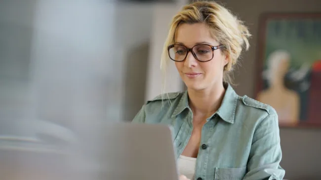 A blonde woman in glasses working on computer.