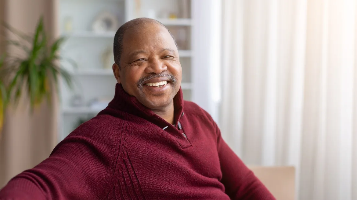 An older man wearing a dark red sweater smiling at the camera.